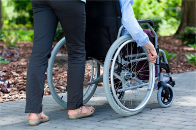 Une aide-soignante poussant une personne âgée en fauteuil roulant.