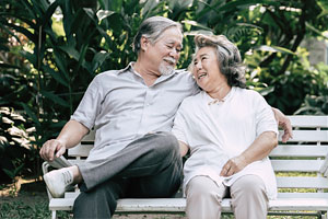 An older couple sit on a bench outside and laugh.