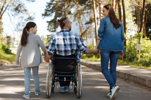 A man using a wheelchair pushes himself beside a walking woman and young girl.