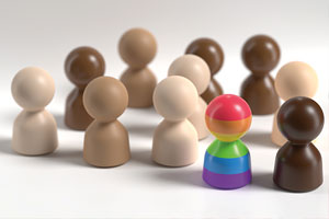 Wooden toys shaped like people in varying skin tones with one that is rainbow coloured.