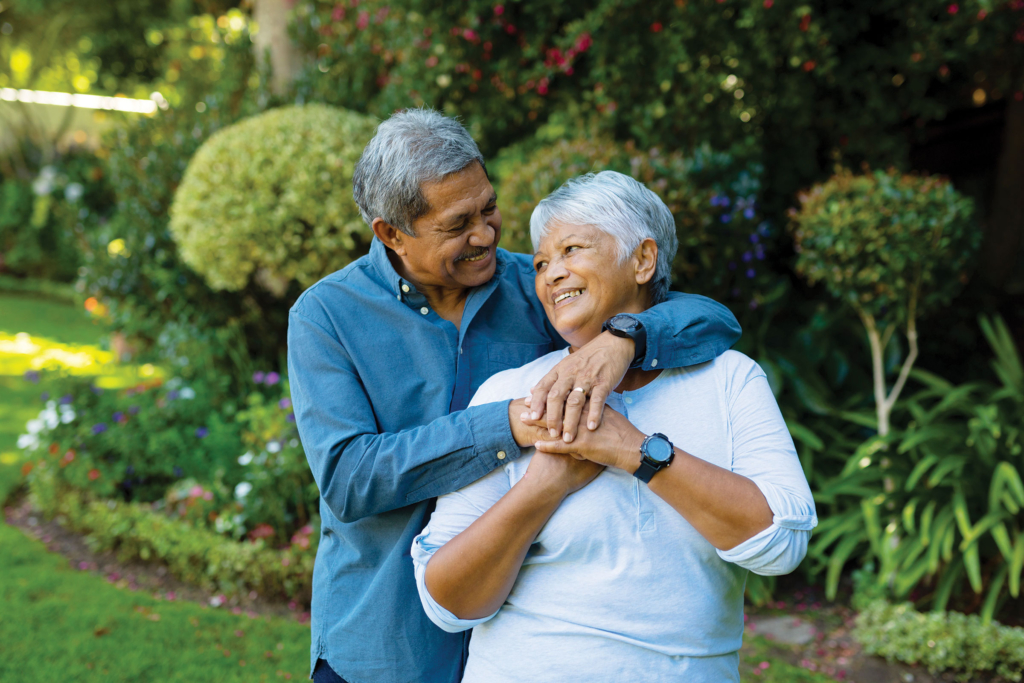 An older couple stand in a garden hugging.